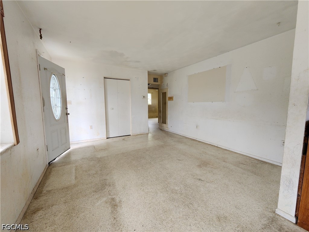 Empty living room with stained carpet, marked walls, and an oval-glass entry door.