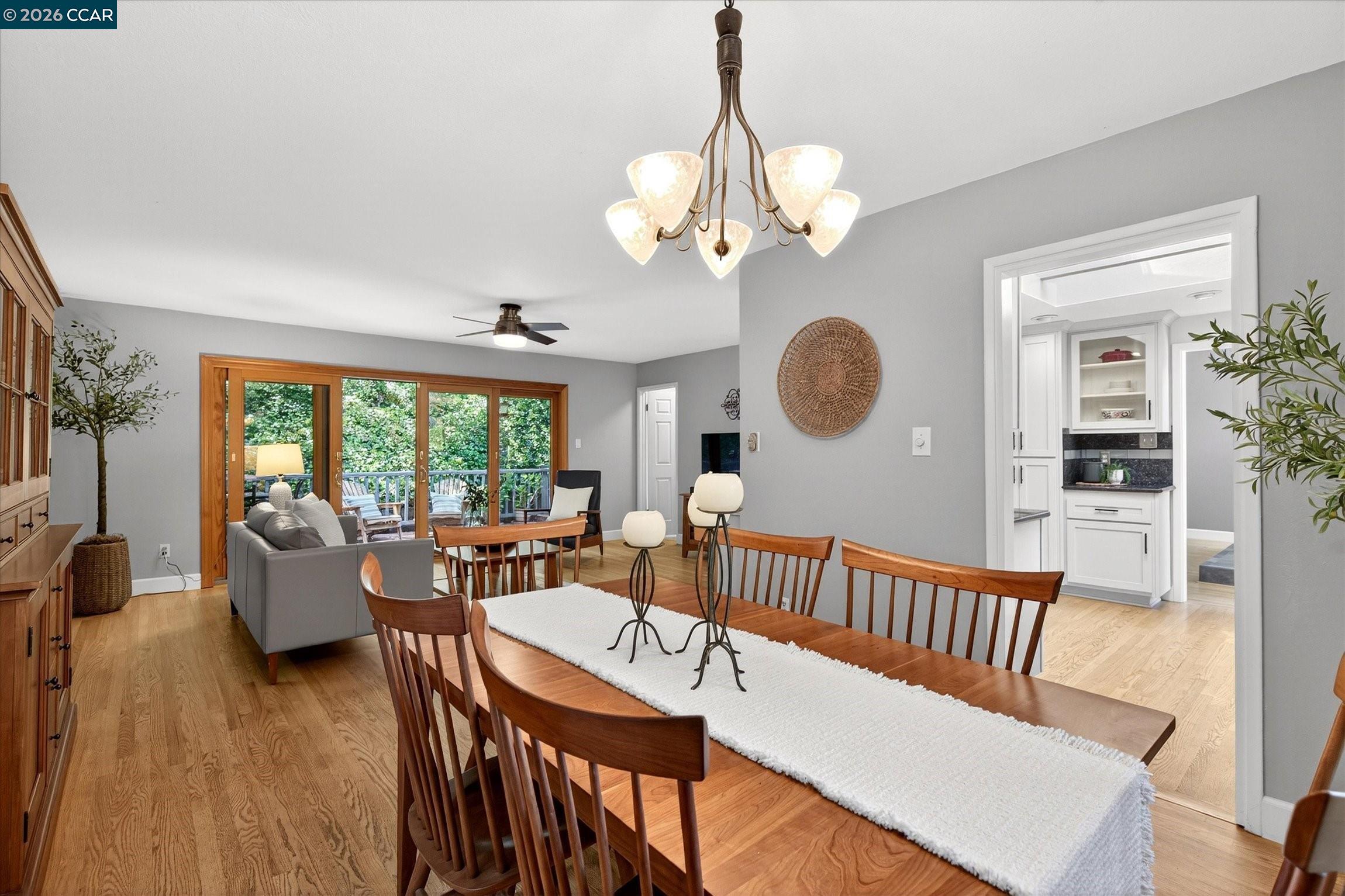 Dining and living area with a long wooden table, hardwood floors, and glass doors to a deck.