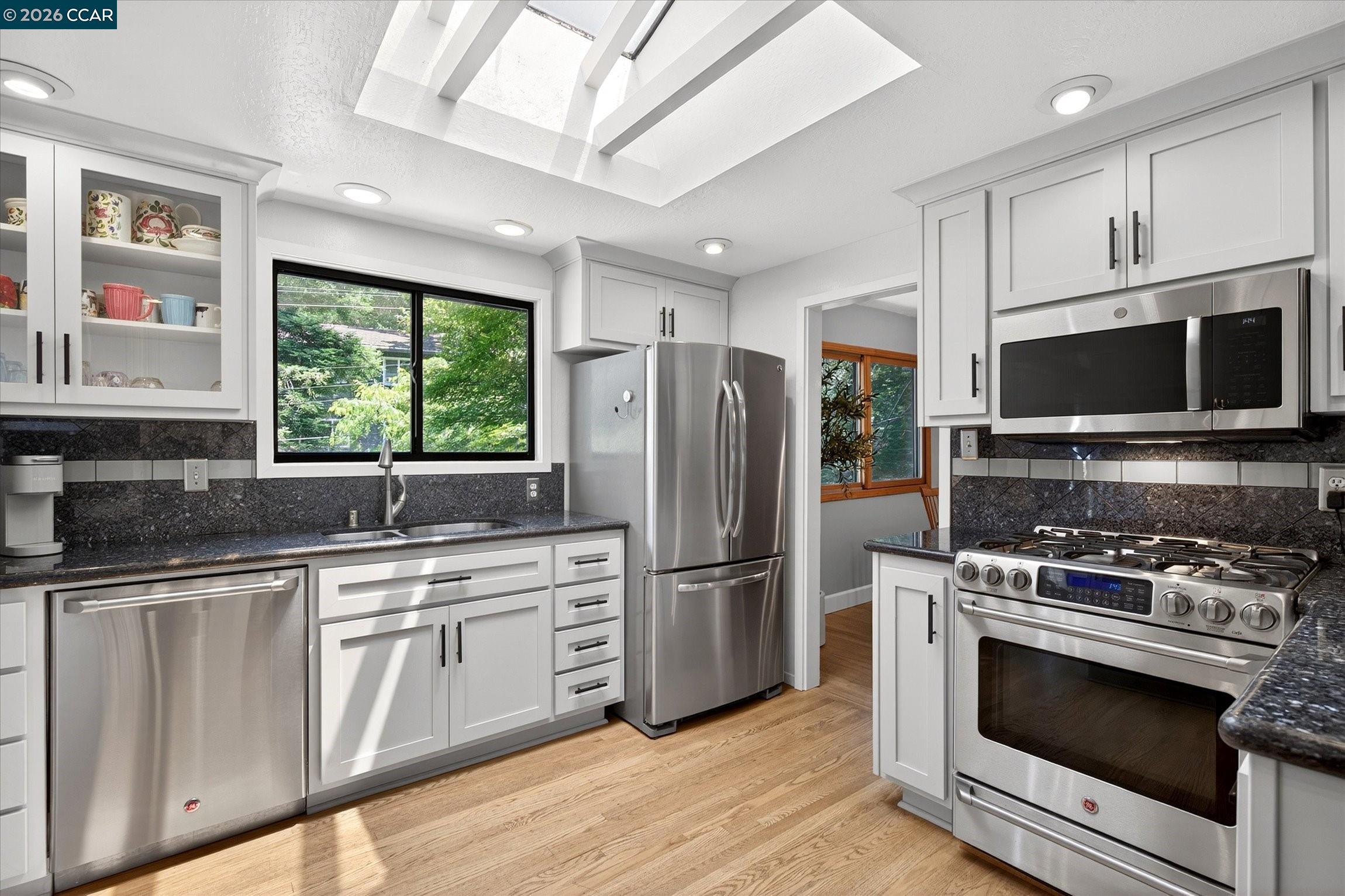 Kitchen with white cabinets, stainless steel appliances, dark stone counters, and a large skylight.