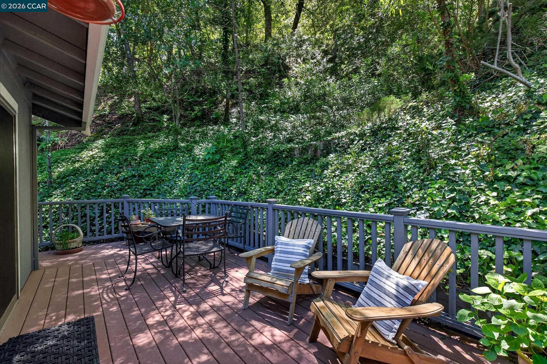Furnished wooden deck with Adirondack chairs overlooking a lush, wooded hillside.