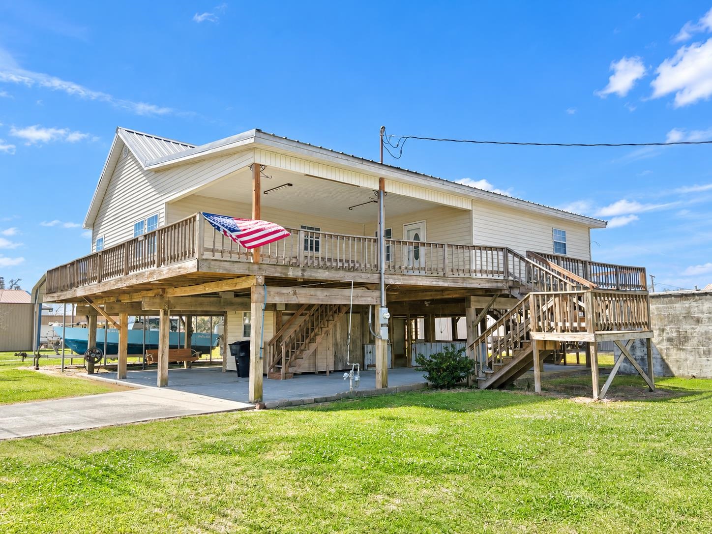 Raised light-colored house with a broad wooden deck, multiple stairways, and an American flag.