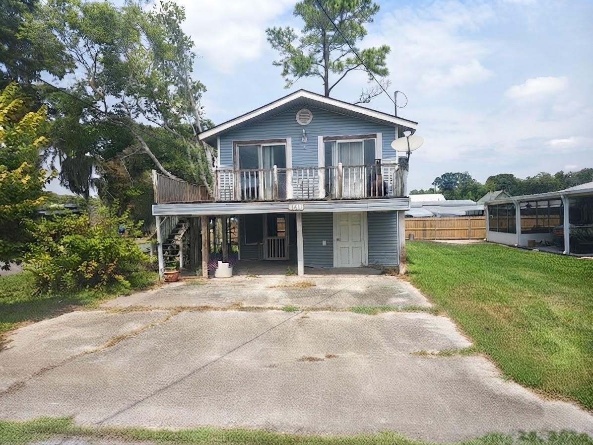 Blue raised house with a white-railed balcony and wide concrete driveway.