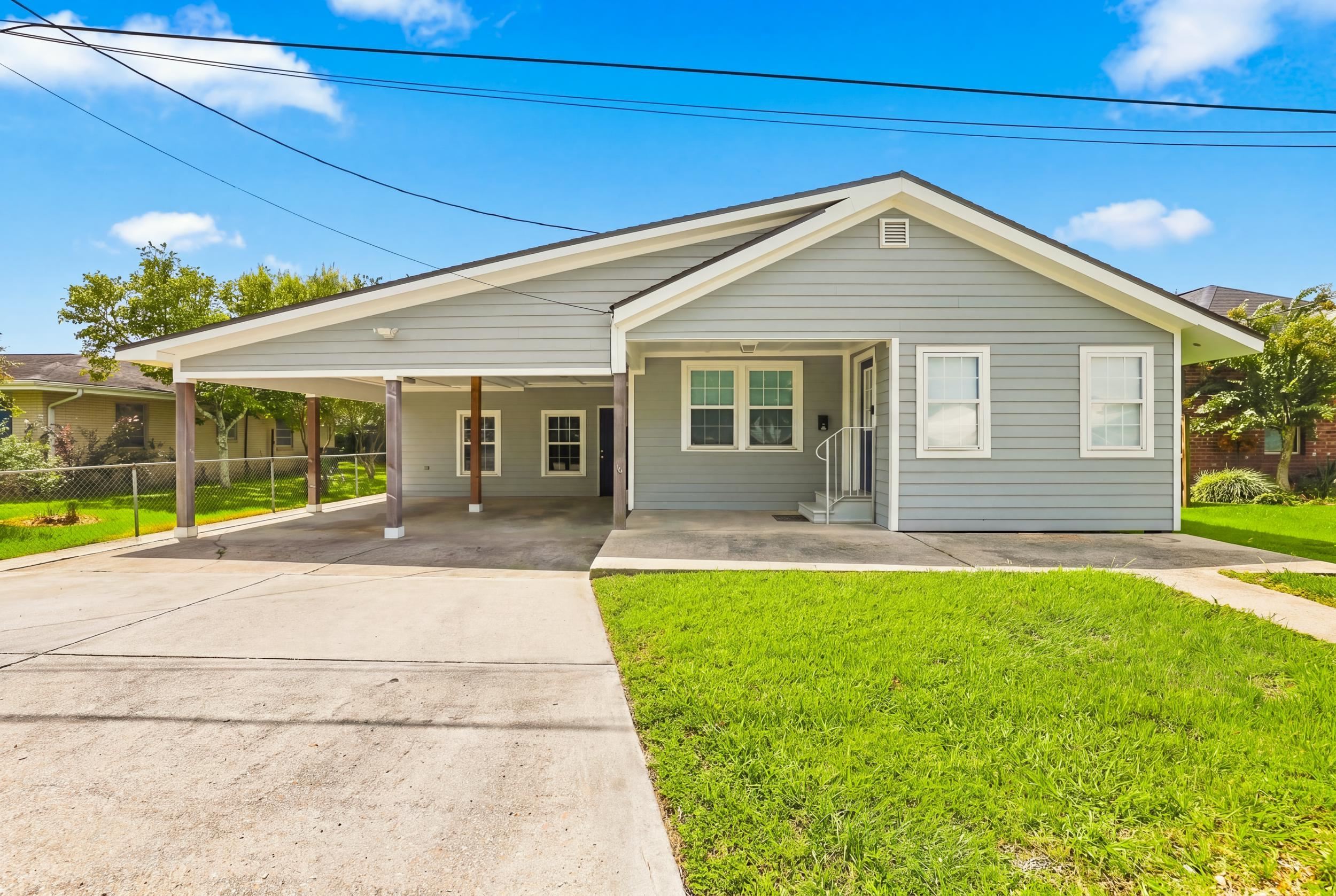 Gray single-story house with a broad covered carport, front porch, and concrete driveway.