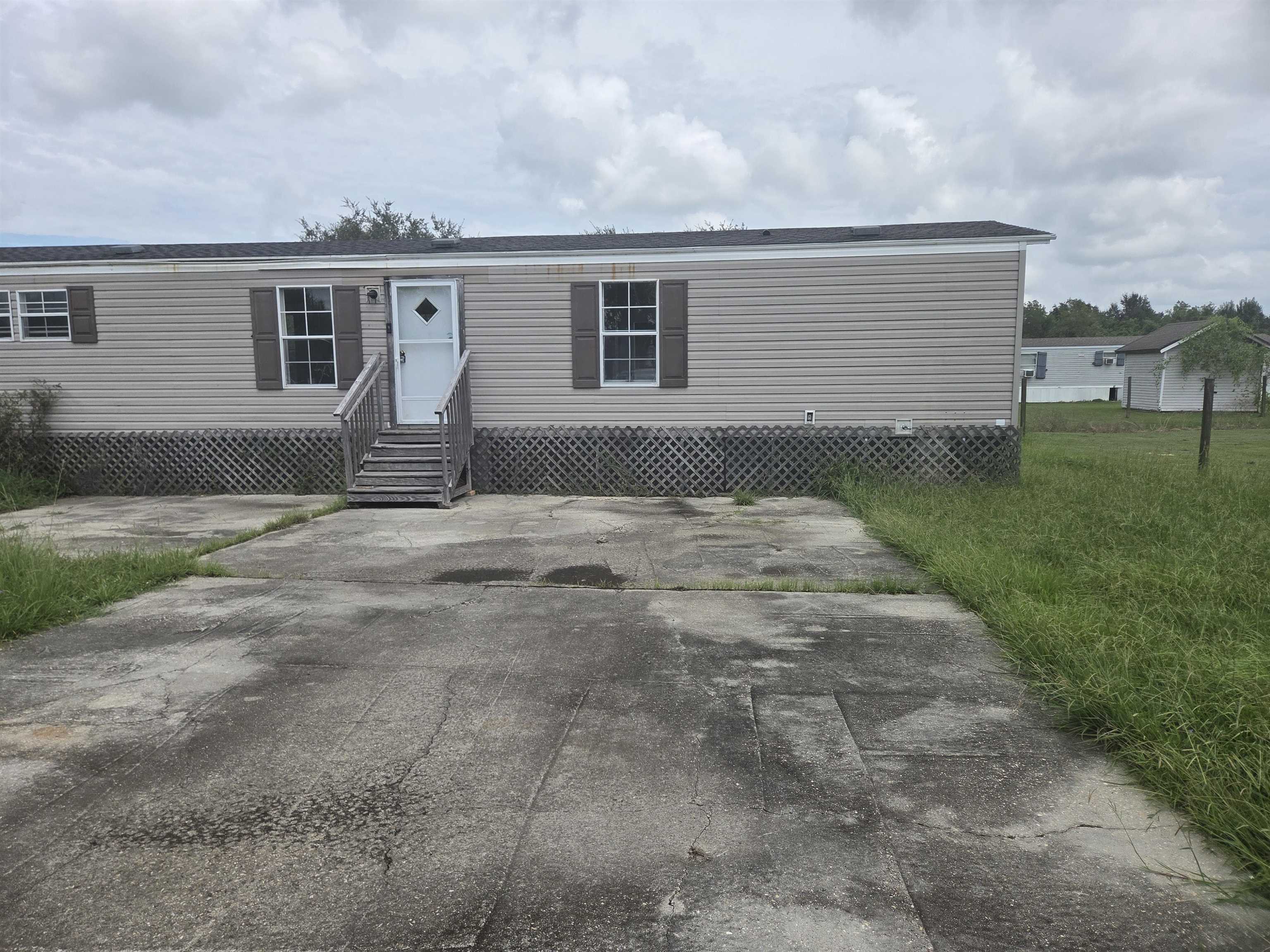 Beige manufactured home with a wooden front stairway and broad cracked concrete driveway.