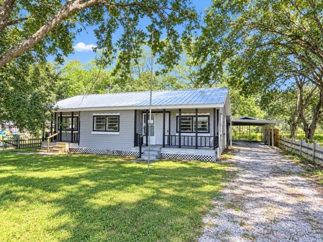 Gray single-story house with a metal roof, covered porch, and gravel driveway to a carport.