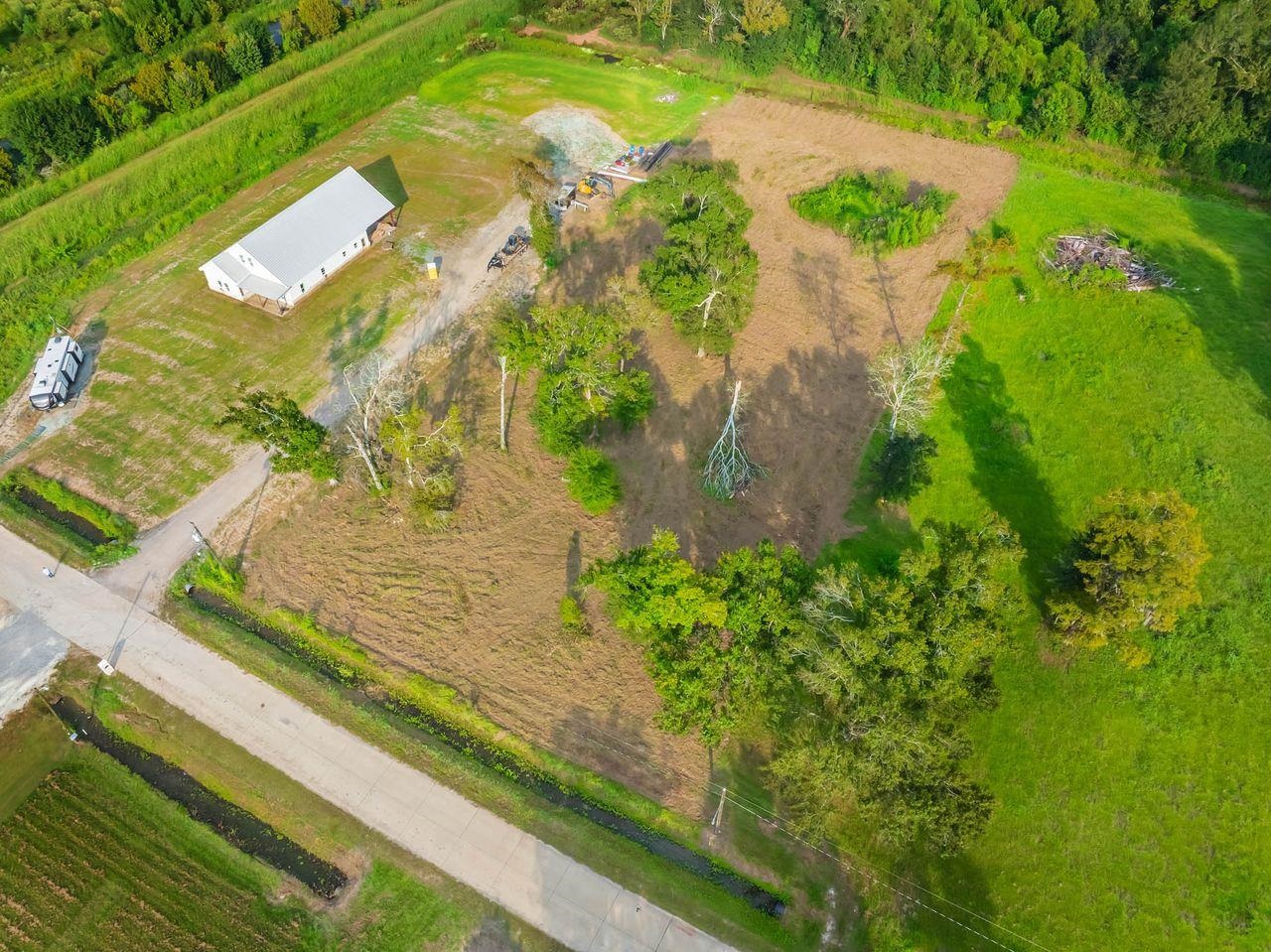 Aerial view of a white metal-roofed building and cleared property surrounded by trees and grass.
