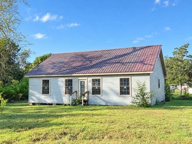 Single-story white house with a reddish-brown metal roof, front windows, and a small porch.