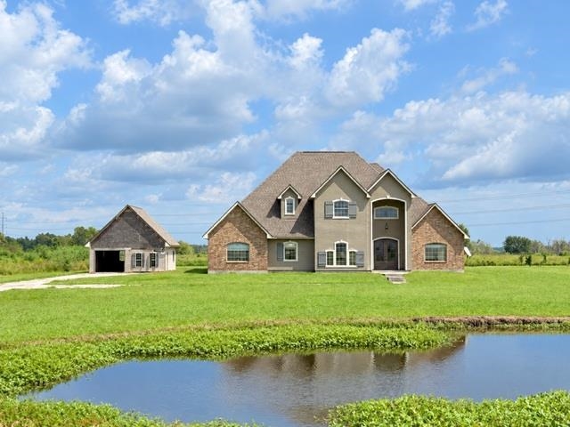 Two-story brick house beside a waterway, with a detached outbuilding and broad green lawn.