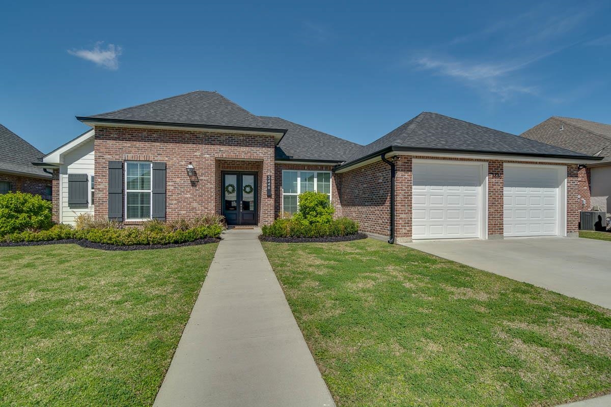 Brick home with a two-car garage, dark shutters, and a walkway through the front lawn.