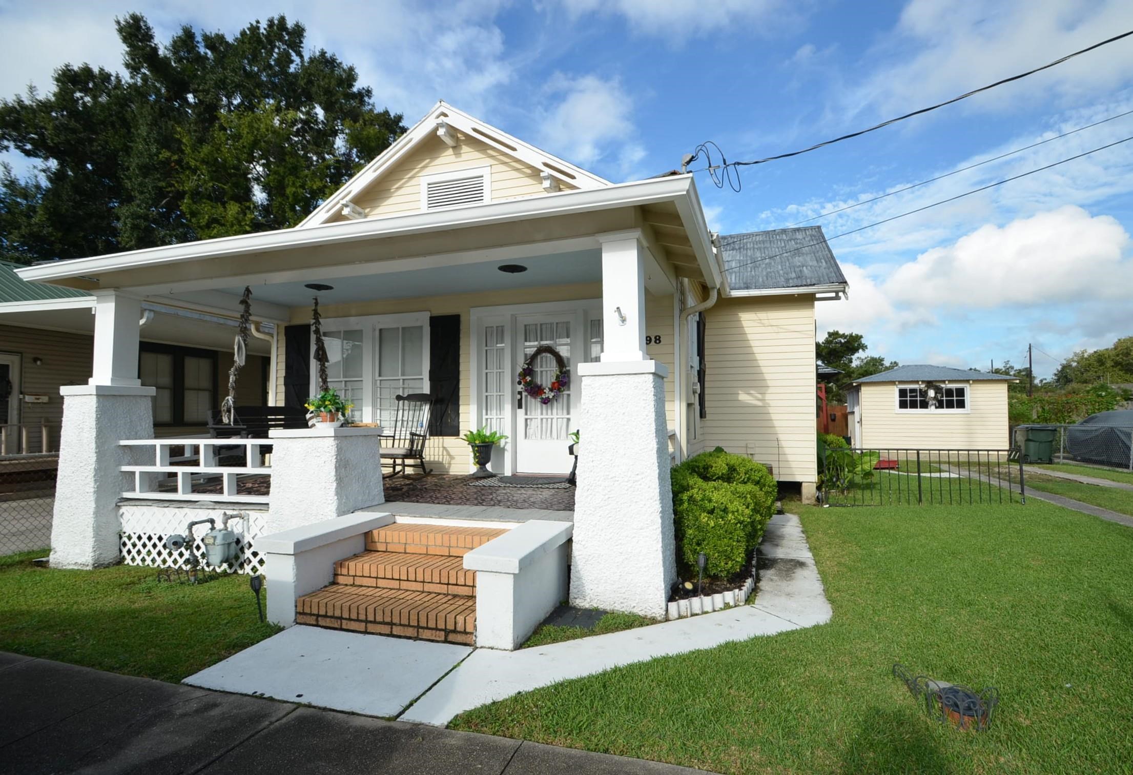 Pale yellow house with a covered porch, brick steps, white columns, and a detached outbuilding.