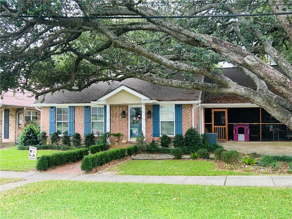 Brick house with blue shutters and a covered carport beneath a sprawling live oak tree.