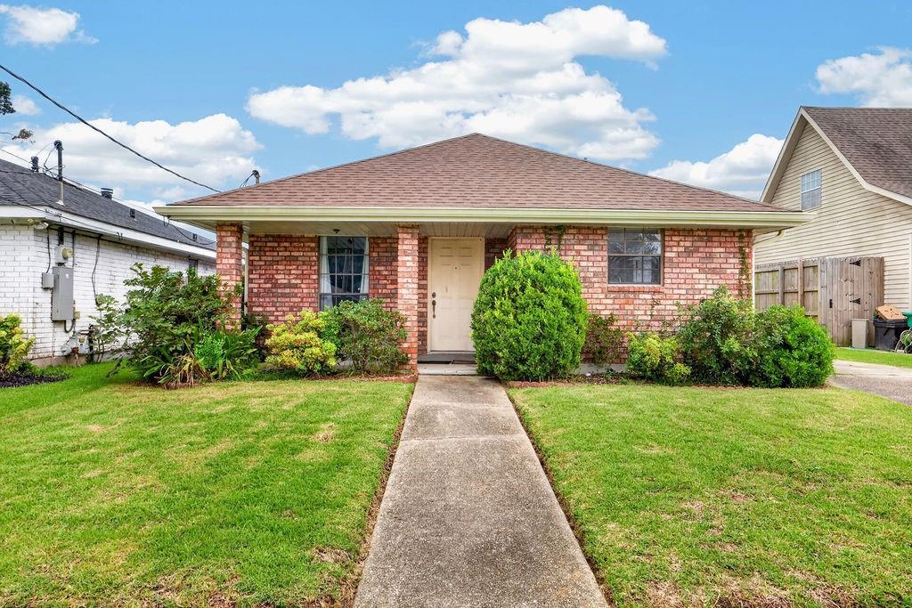 Single-story brick house with a central walkway, front lawn, and neatly trimmed shrubs.