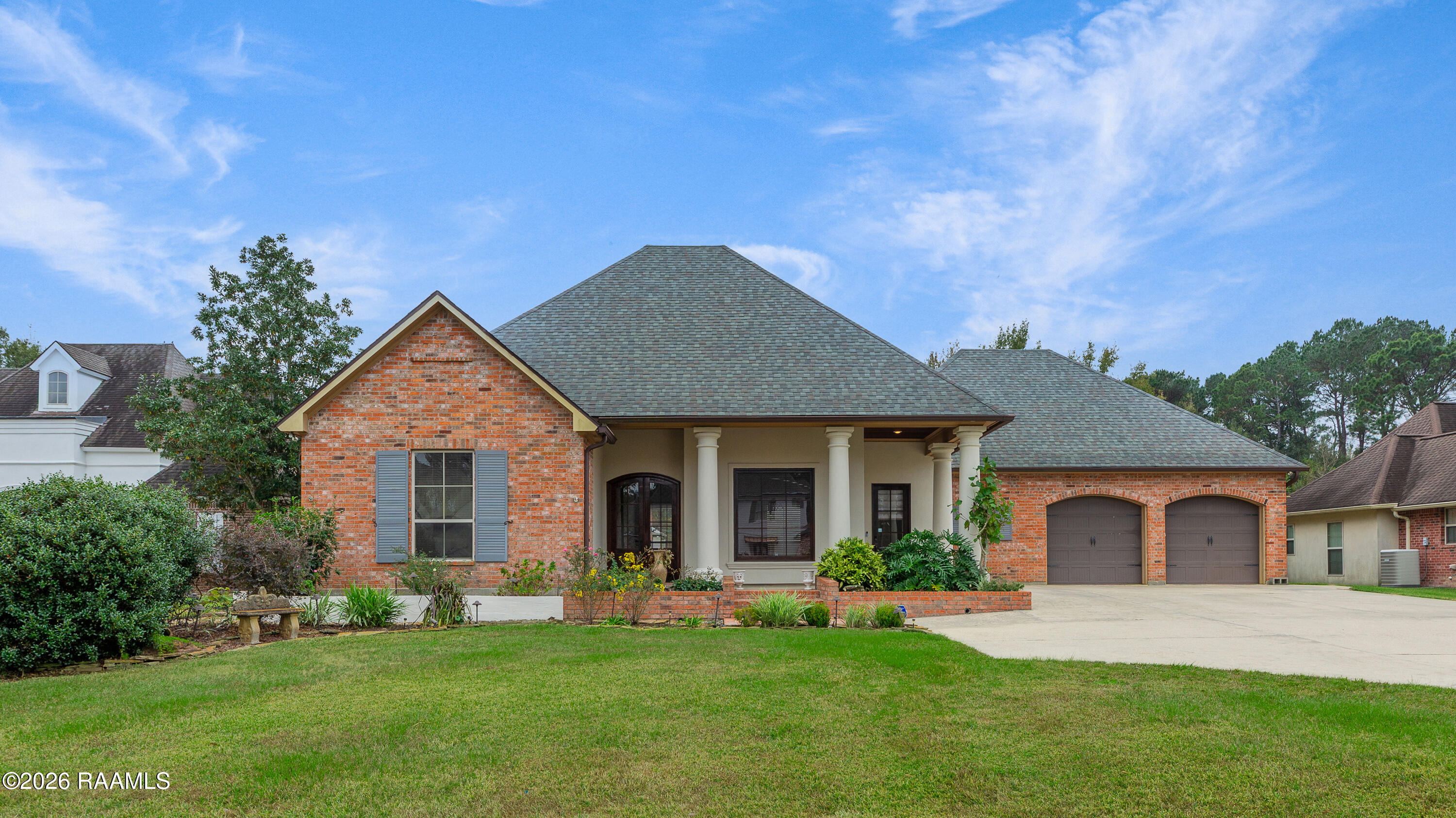 Brick house with a columned porch, double garage, landscaped beds, and broad front lawn.