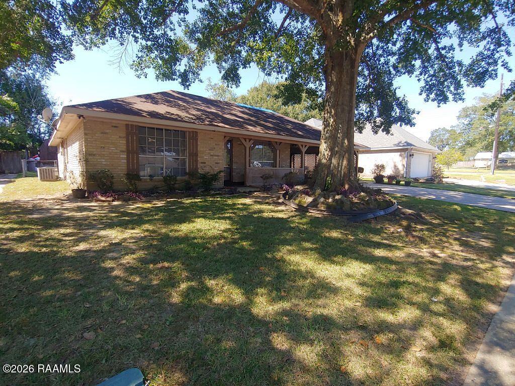 Single-story brick house with a covered porch beneath a large shade tree.