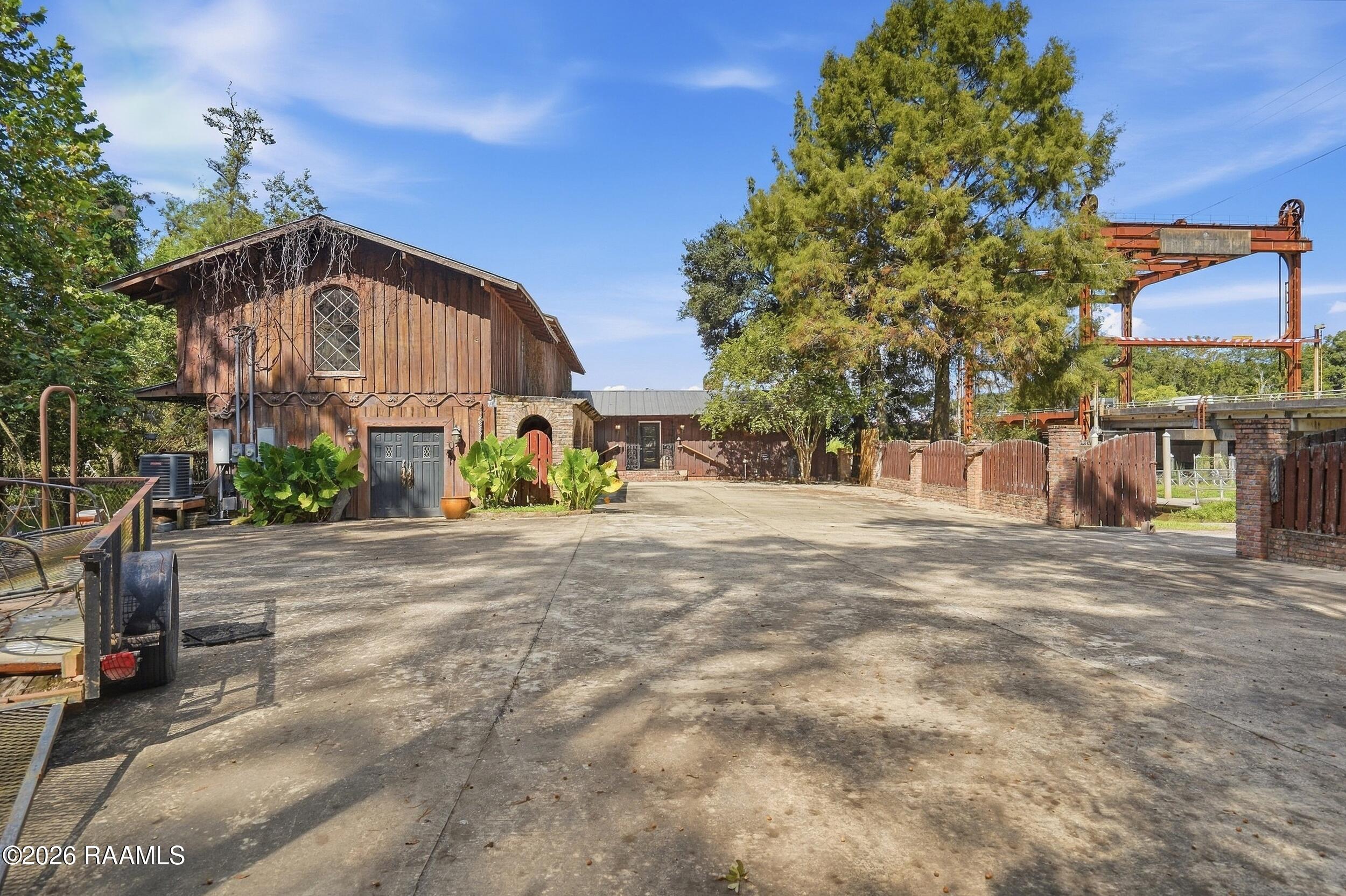 Rustic wood-and-stone building beside a wide paved courtyard and rust-colored industrial gantry.
