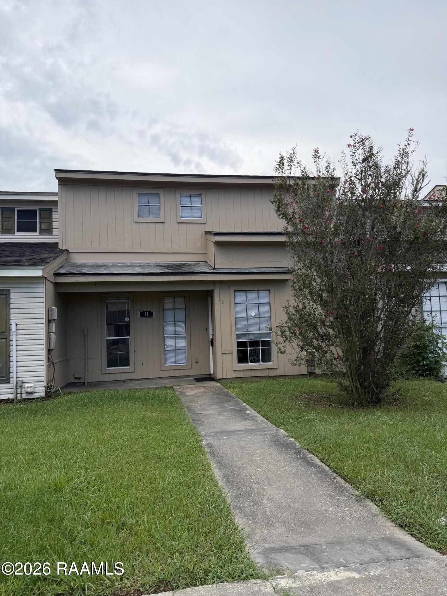 Beige two-story townhouse with a covered entry, number 11, walkway, and flowering tree.