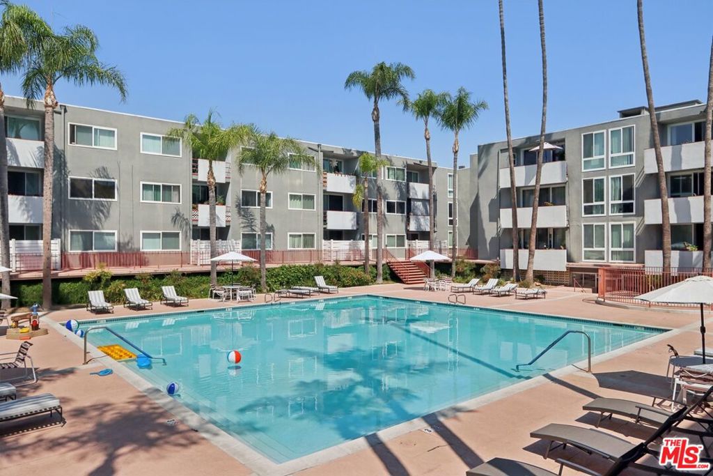 Apartment building surrounding a swimming pool, with palm trees and lounge chairs.