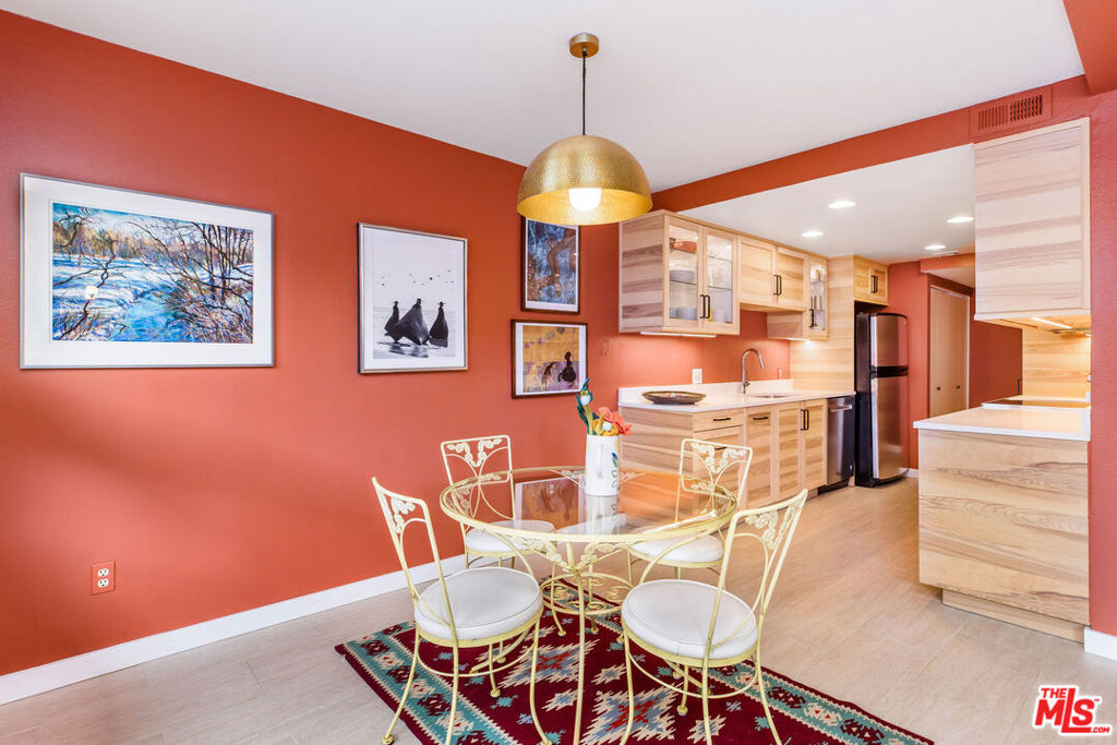 Dining area with a glass table and white chairs beside a light wood kitchen.