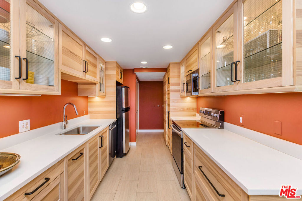Kitchen with light wood cabinets, glass-front cupboards, white counters, and orange walls.