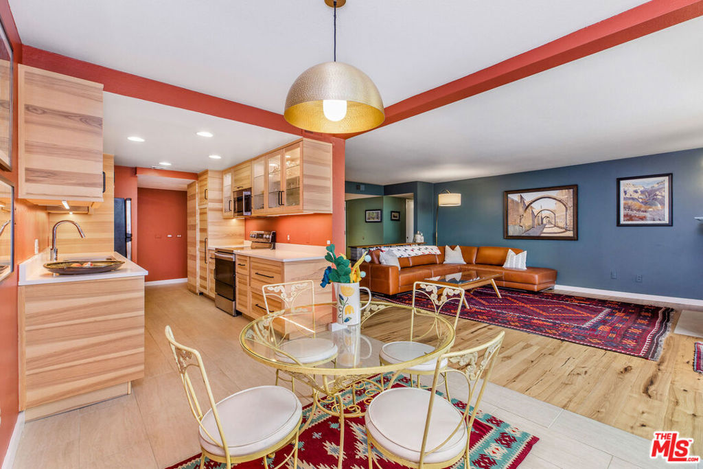 Open-plan kitchen and living area with light wood cabinetry, a glass dining table, and brown sectional.