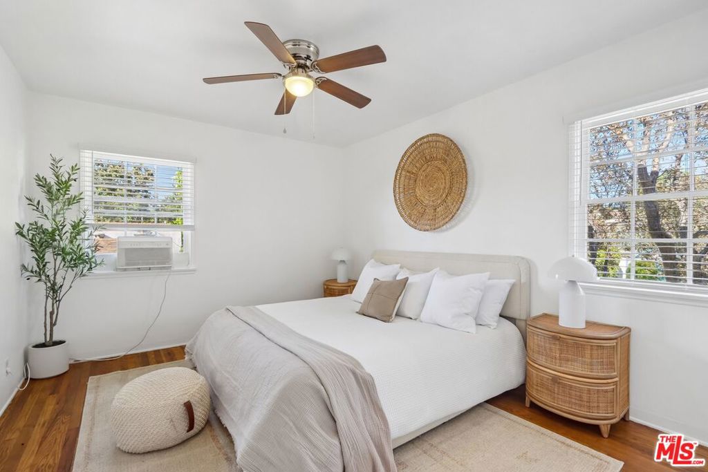 Bright bedroom with a white bed, woven wall decor, and windows on two walls.