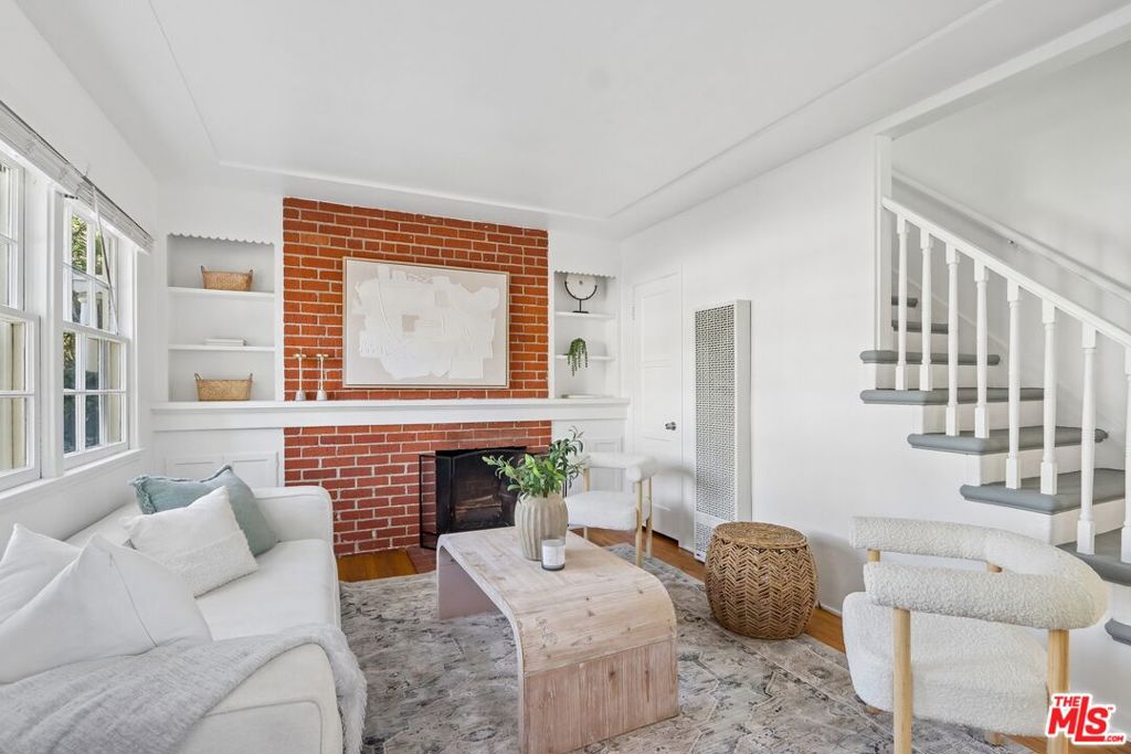 Living room with a red brick fireplace, white seating, large windows, and a staircase.