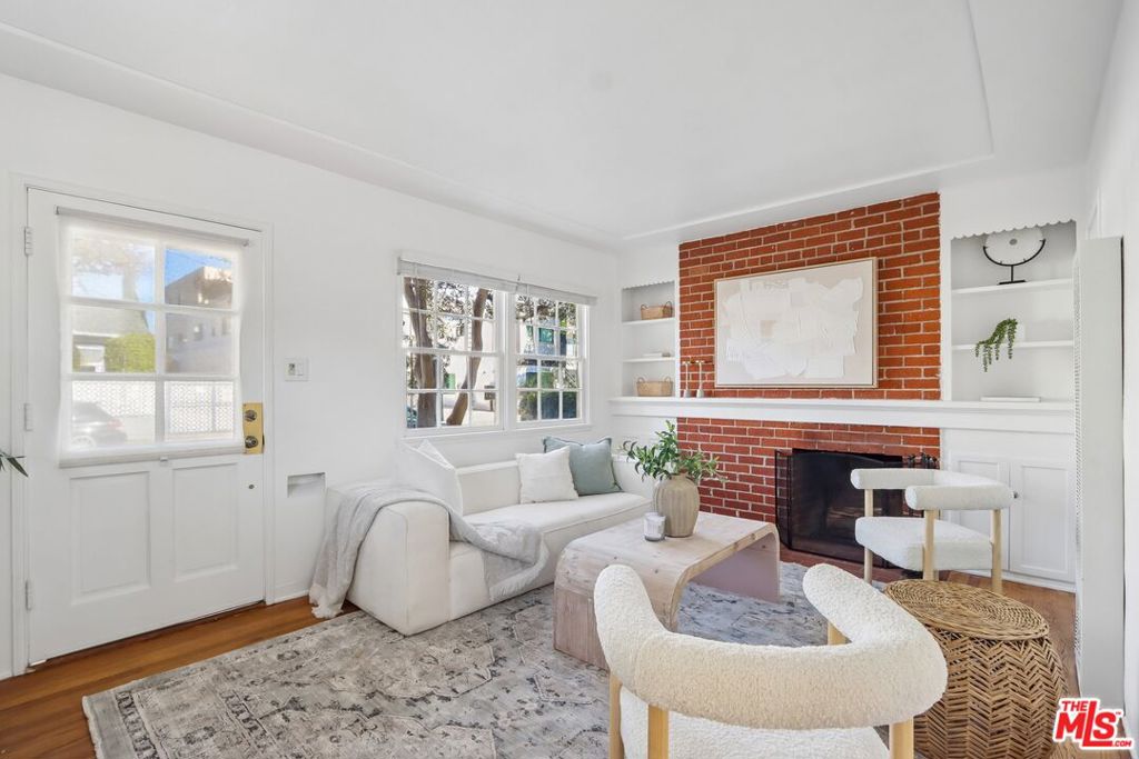 Furnished living room with a red brick fireplace, white seating, and built-in shelves.