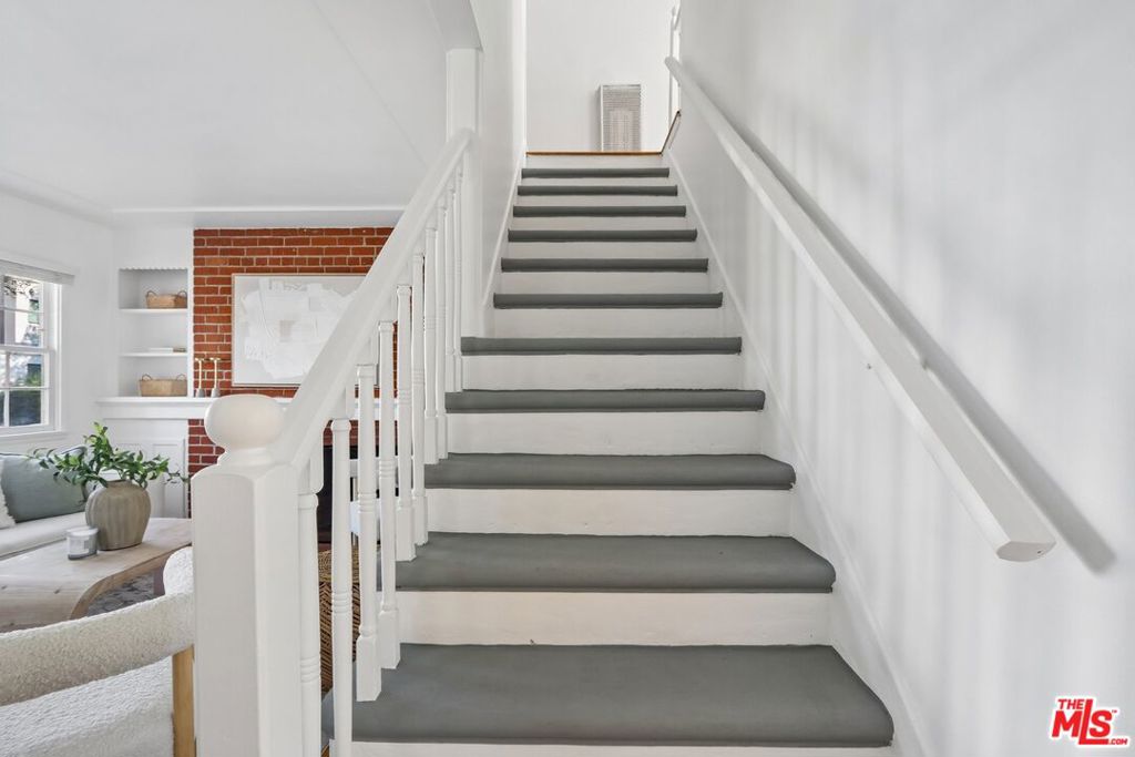 White staircase with gray treads beside a living area with a red brick accent wall.