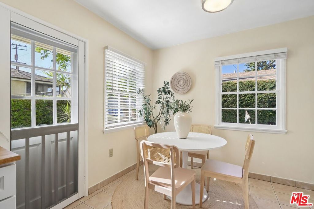 Dining nook with a round white table, woven chairs, and windows overlooking greenery.
