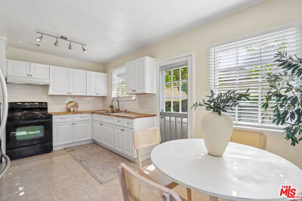 Bright kitchen with white cabinets, butcher-block counters, and a round dining table by large windows.
