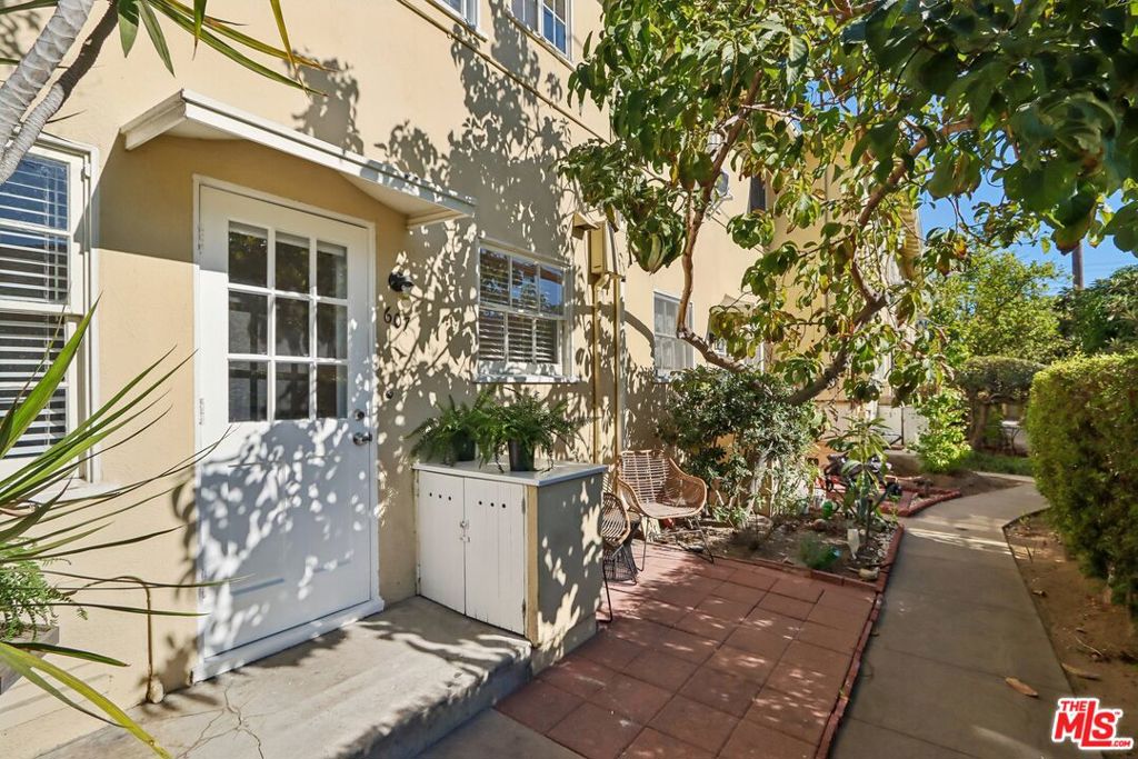 Building-side patio with a white glass-paneled door, outdoor chairs, and a garden path.