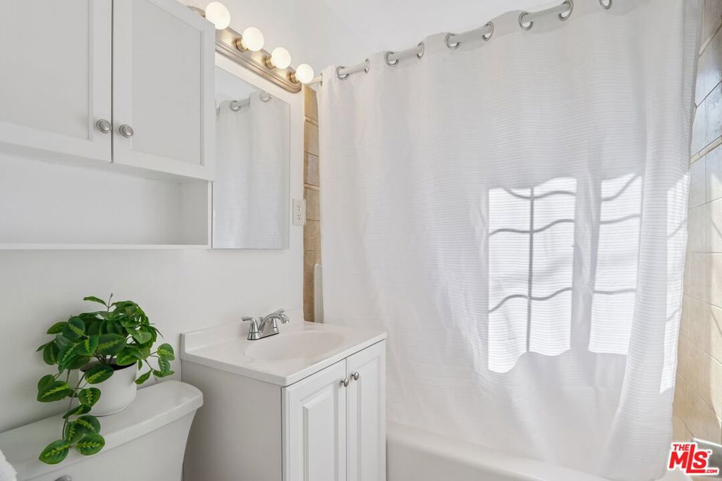 Bathroom with a white vanity, mirrored medicine cabinet, and sheer curtain over the tub.