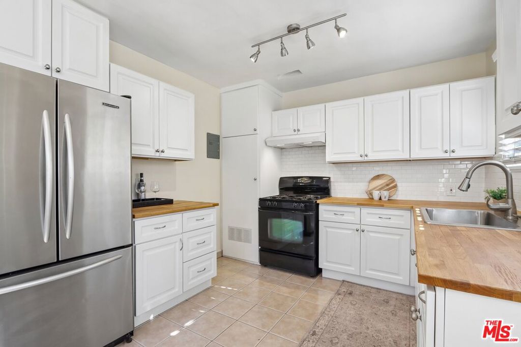 Kitchen with white cabinets, butcher-block counters, stainless refrigerator, and black range.