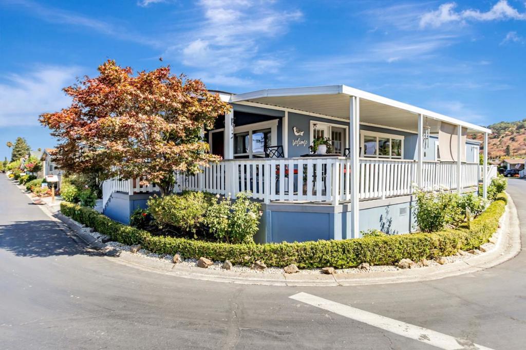 Blue single-story home with a broad white covered porch and an autumn tree.