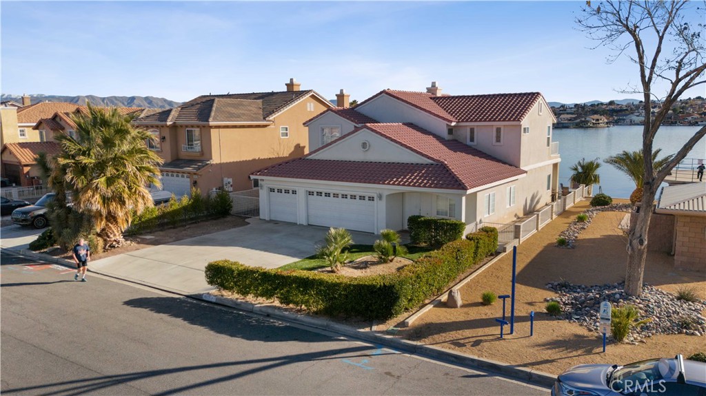 Two-story waterfront home with a red tile roof, three-car garage, and landscaped front yard.