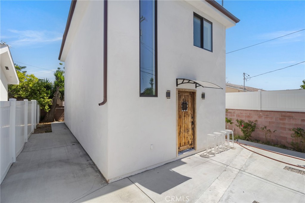 White stucco home with a wood entry door, narrow windows, and paved side yard.