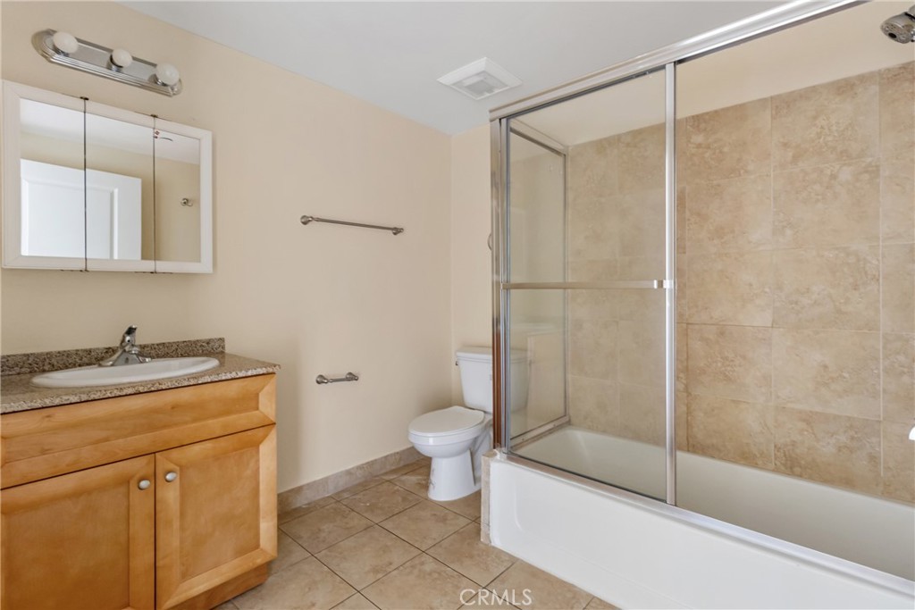 Bathroom with a wood vanity and a beige-tiled bathtub enclosed by sliding glass doors.