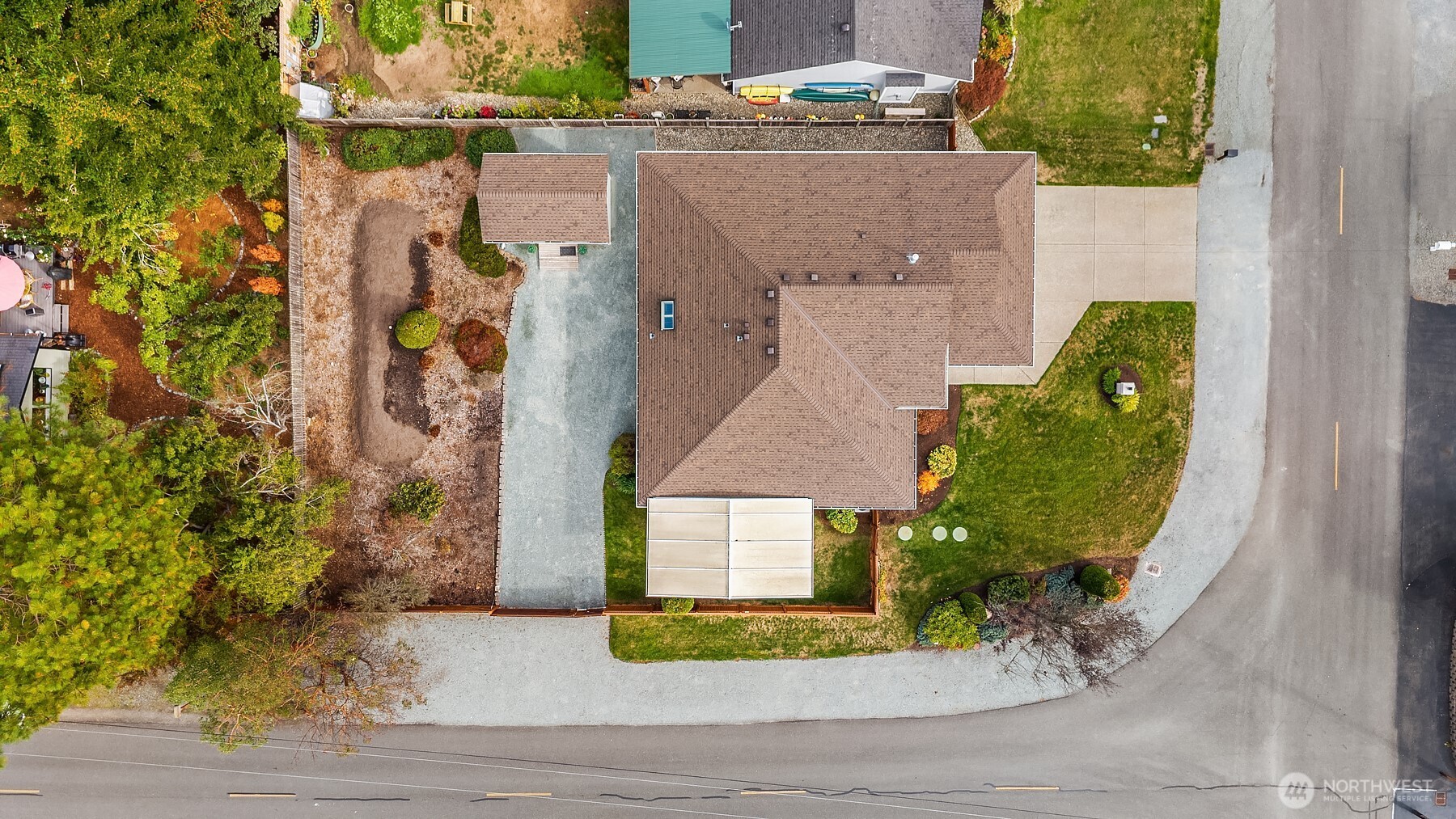 Aerial view of a brown-roofed home on a landscaped corner lot with a wide driveway.