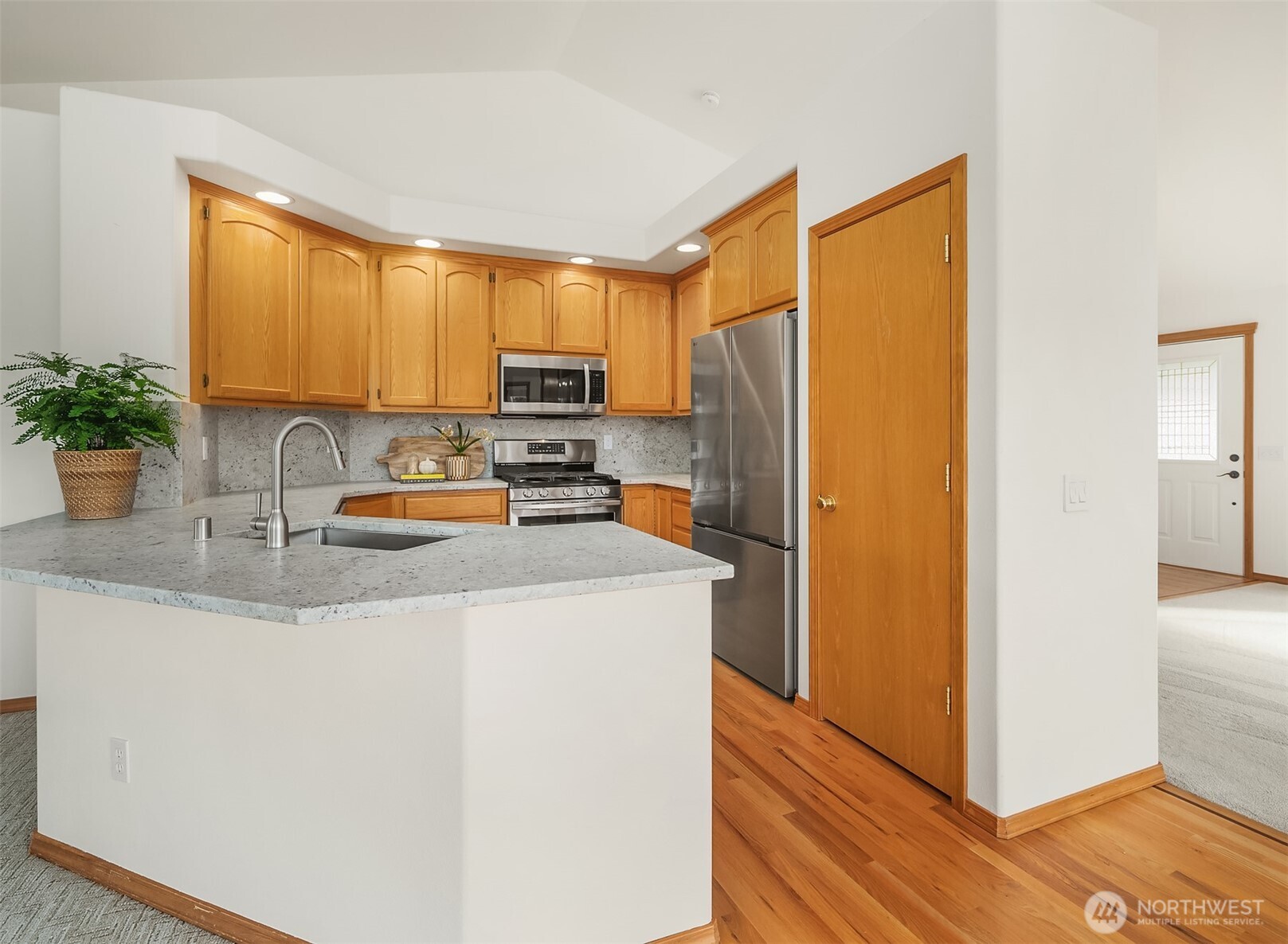 Kitchen with honey-colored wood cabinets, stainless steel appliances, and a gray stone peninsula.