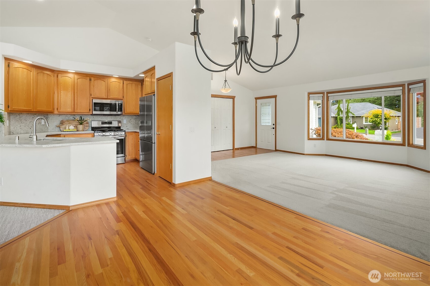 Open kitchen and living area with honey-toned cabinetry, hardwood floors, and large windows.