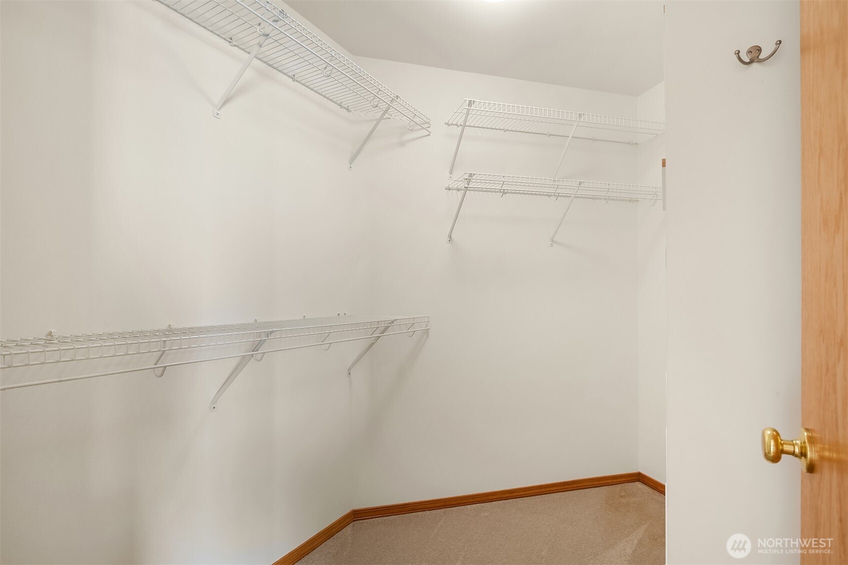 Empty walk-in closet with white wire shelves, beige carpet, and an open wooden door.
