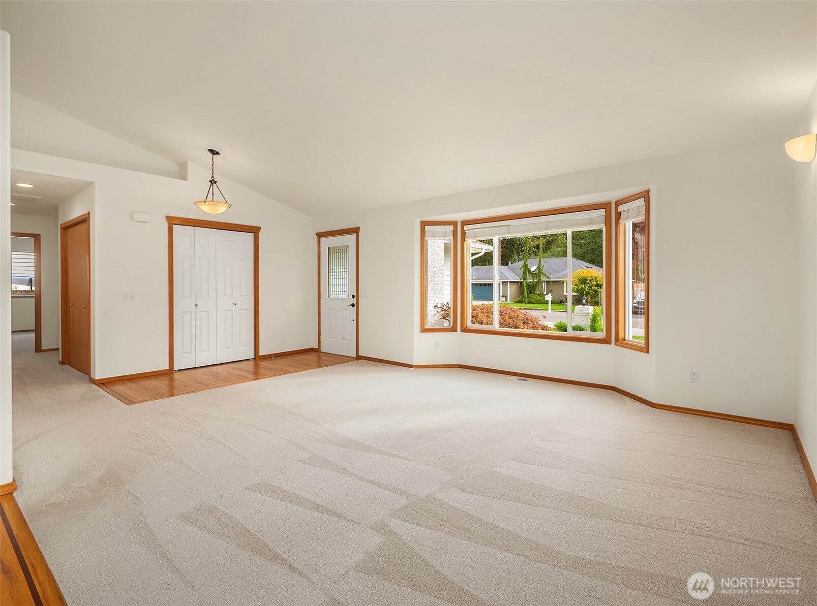 Vacant carpeted room with warm wood trim, double closet doors, and a large bay window.