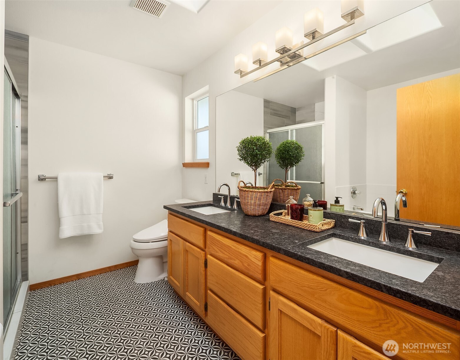 Bathroom with a double-sink wood vanity, patterned tile floor, and glass shower.