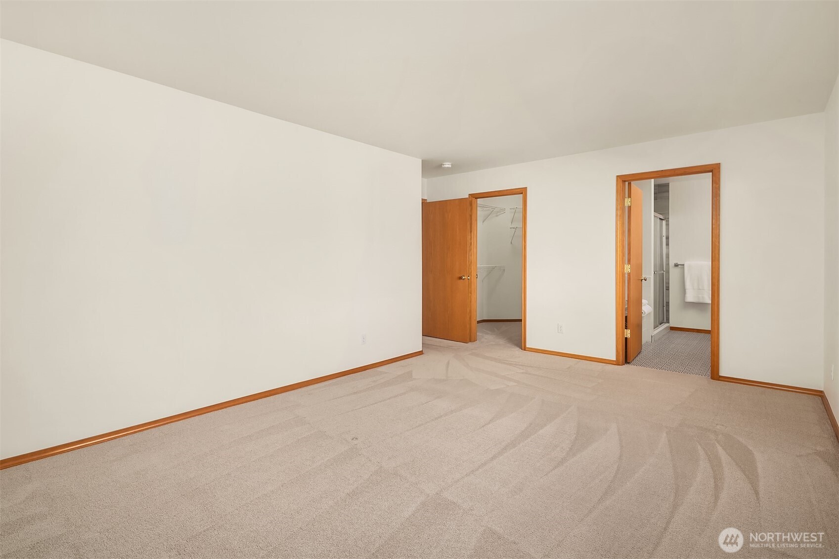 Empty carpeted bedroom with wood-trimmed doors to a closet and adjoining bathroom.