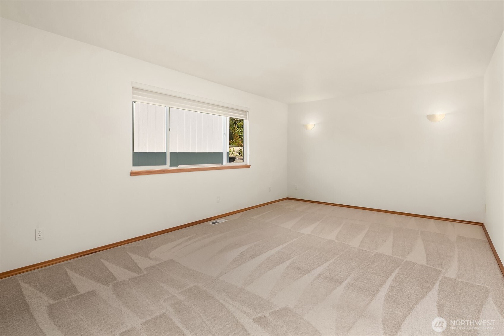 Vacant bedroom with patterned carpet, a wide window, and two wall sconces.