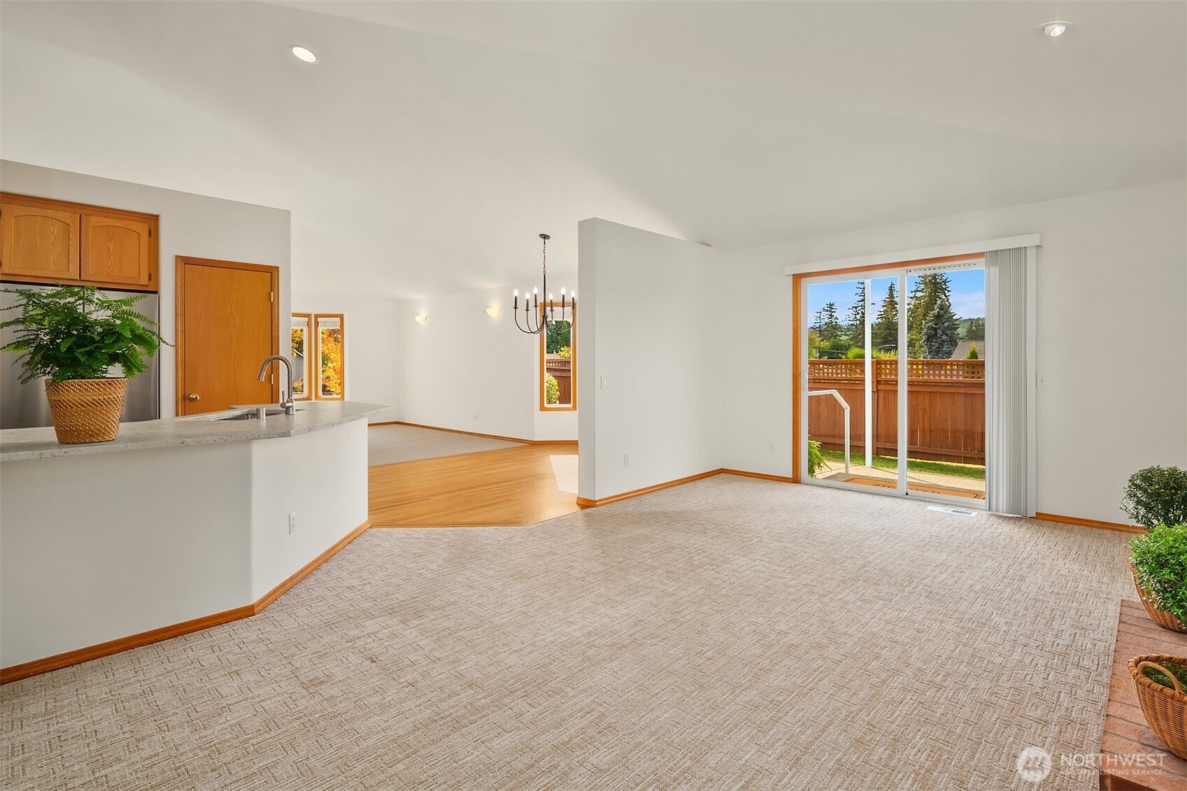 Open living and dining area with beige carpet, wood-trimmed kitchen, and sliding doors to a deck.