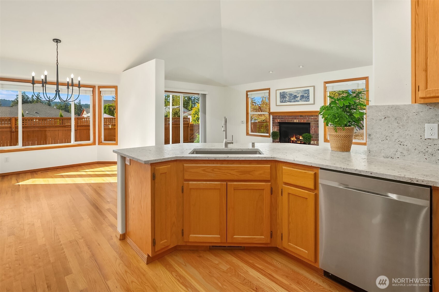 Kitchen with a large stone island, warm wood cabinetry, hardwood floors, and a brick fireplace.