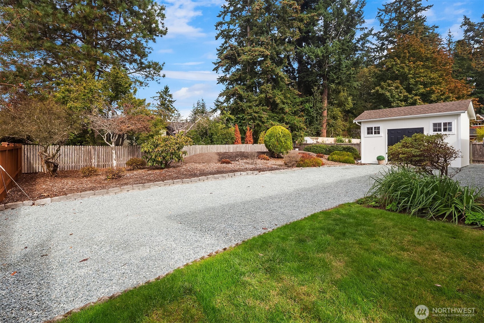 Landscaped yard with a gravel driveway, green lawn, and white detached shed.
