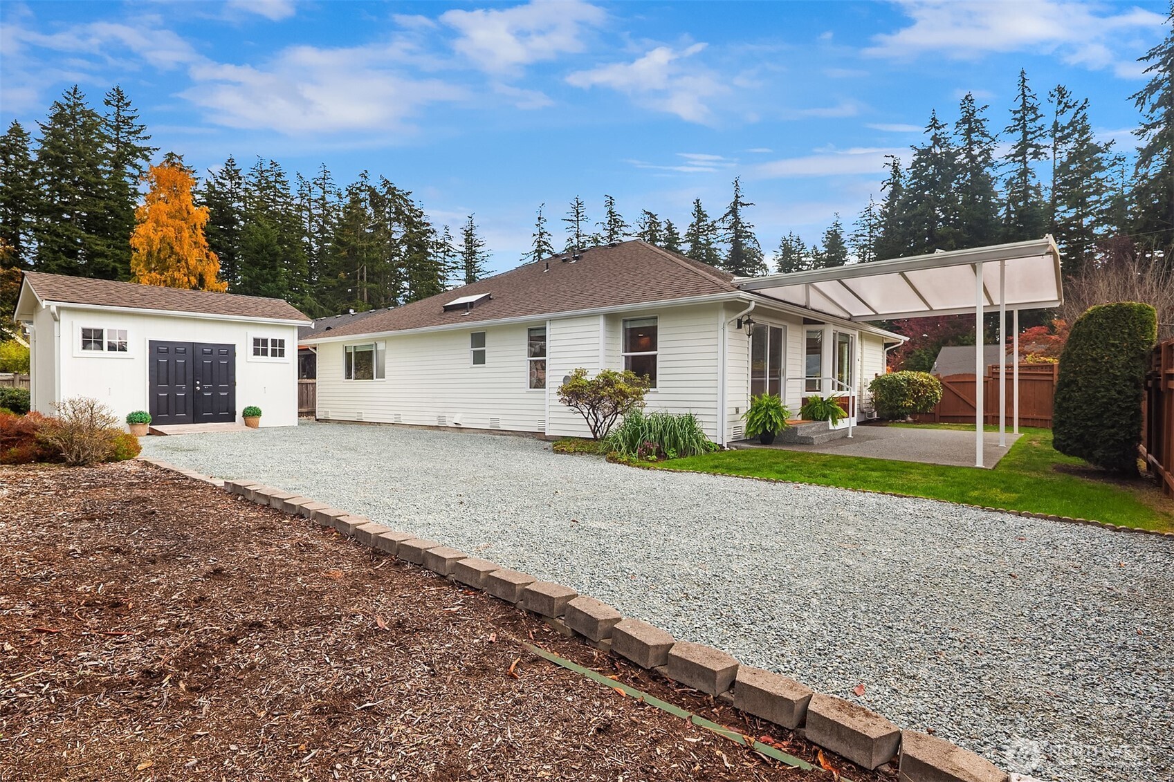 White single-story home with detached garage, gravel driveway, and covered patio.
