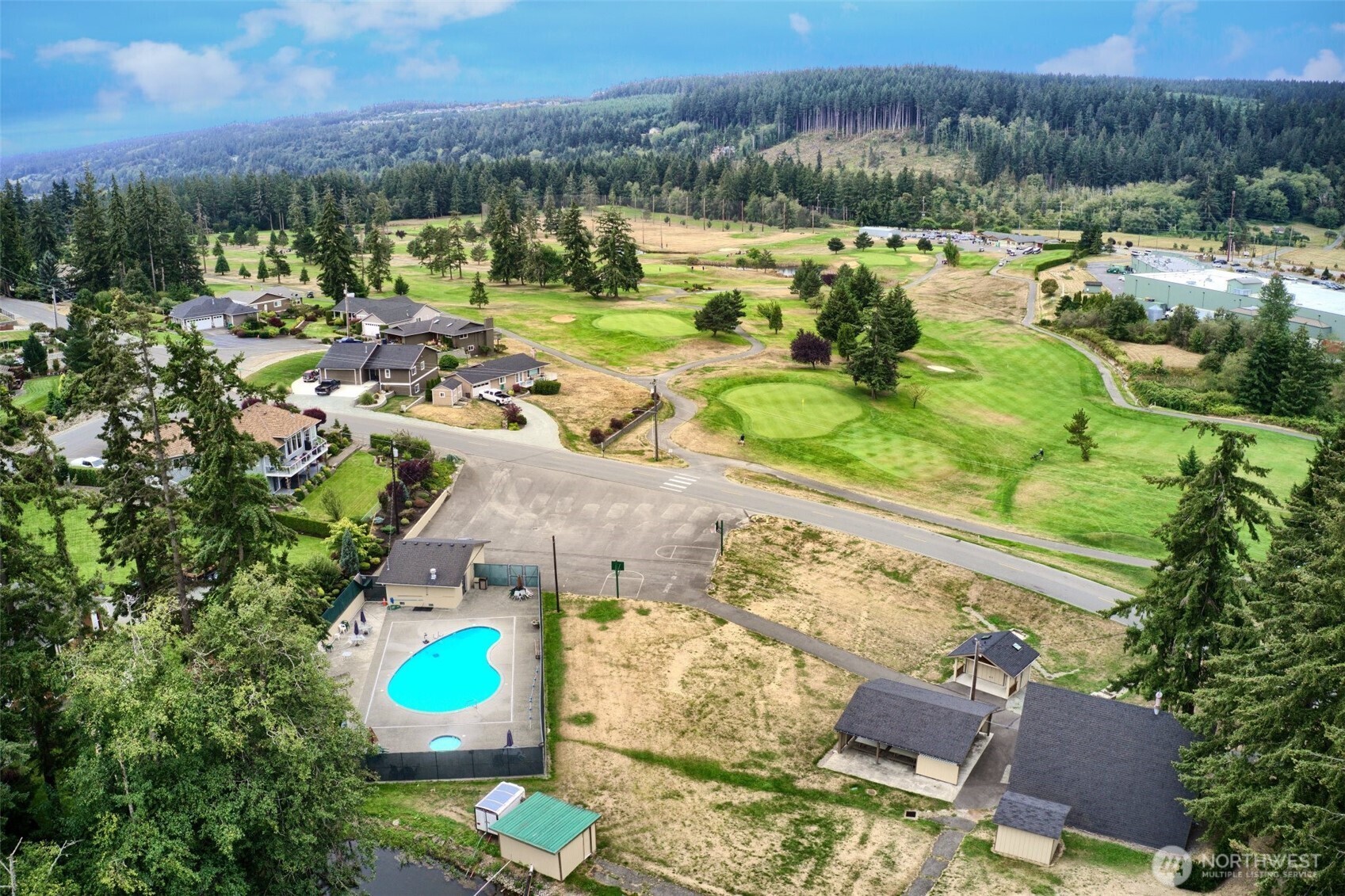Aerial view of homes bordering a golf course, with a swimming pool and wooded hills beyond.